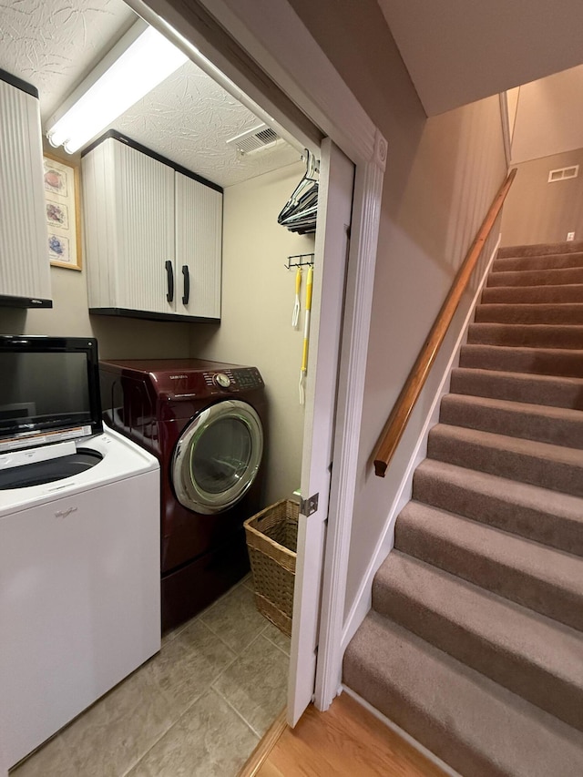 laundry area with washer and dryer, a textured ceiling, and cabinets