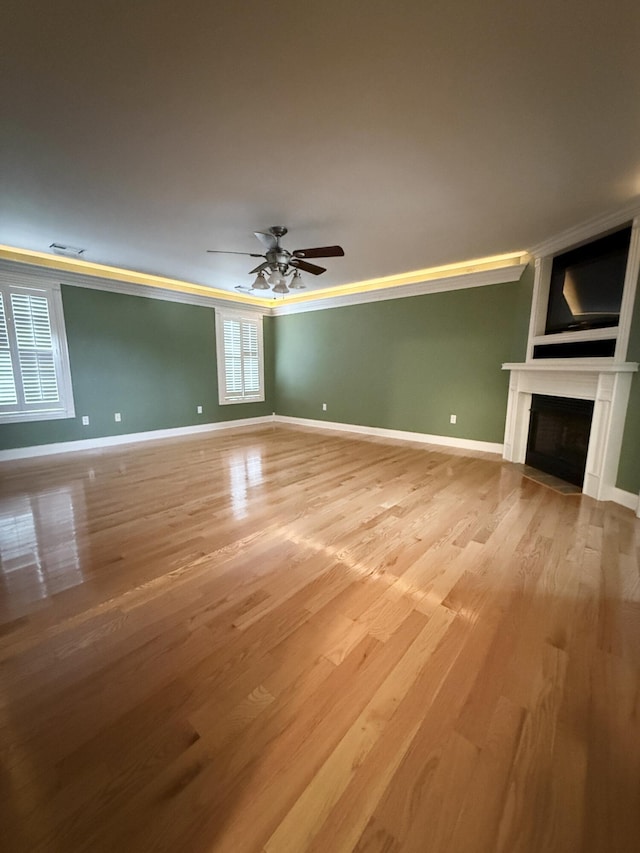 unfurnished living room featuring ceiling fan, wood-type flooring, and ornamental molding