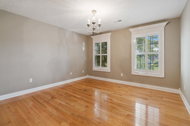 unfurnished room with a textured ceiling, light hardwood / wood-style flooring, and a notable chandelier