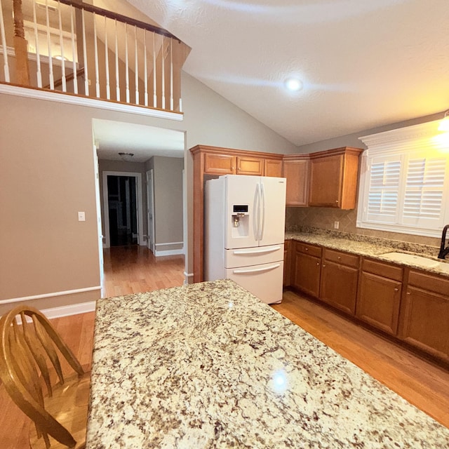 kitchen featuring white refrigerator with ice dispenser, backsplash, sink, vaulted ceiling, and light wood-type flooring