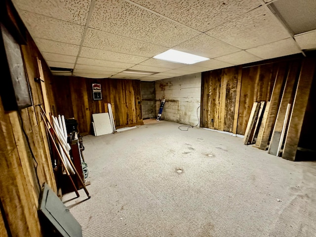 basement with a paneled ceiling, carpet floors, and wooden walls