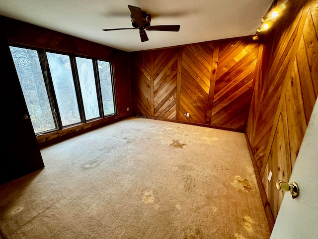 carpeted spare room with ceiling fan and wood walls