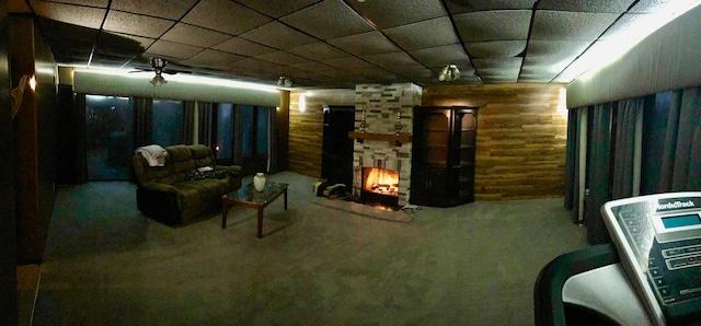 basement featuring wooden walls, a fireplace, carpet, and ceiling fan