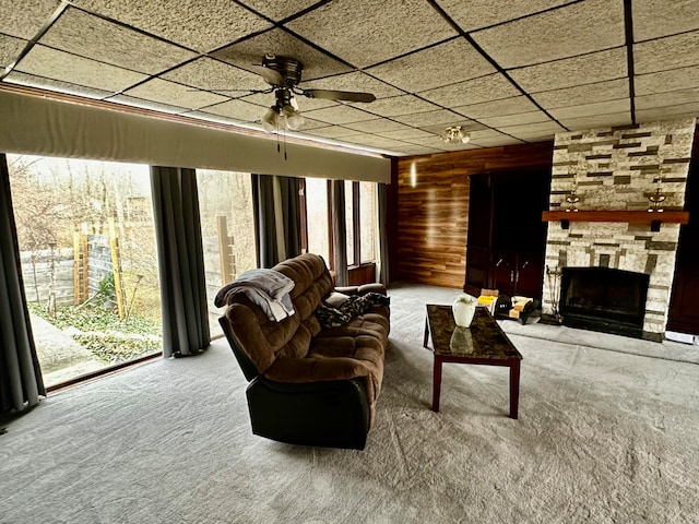 carpeted living room with wooden walls, a fireplace, ceiling fan, and a healthy amount of sunlight