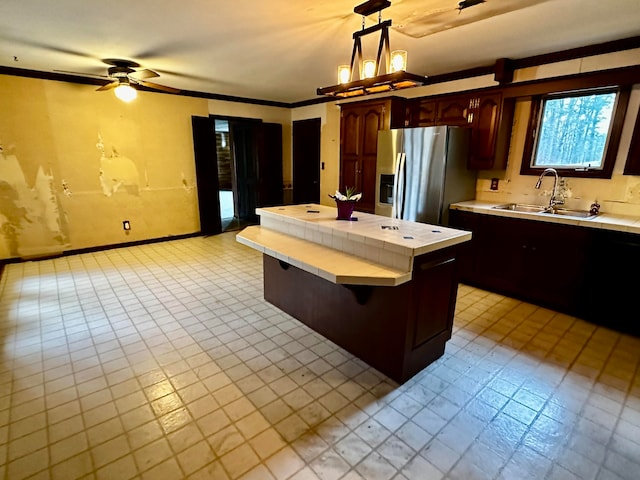 kitchen with sink, ceiling fan, stainless steel fridge, decorative light fixtures, and a kitchen island