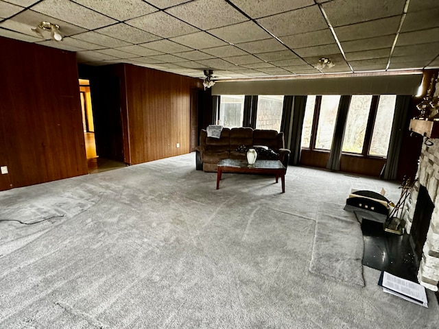 carpeted living room with a paneled ceiling, wood walls, a fireplace, and ceiling fan