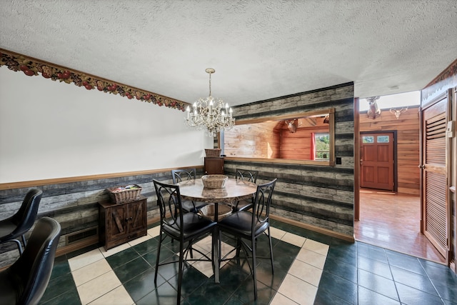 tiled dining area featuring a notable chandelier, wood walls, and a textured ceiling