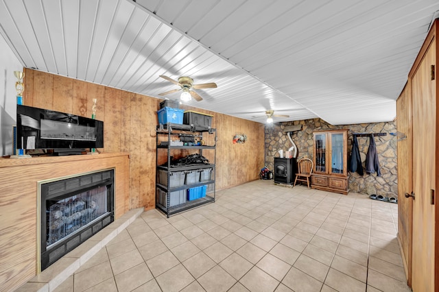 living room featuring wood ceiling, a wood stove, ceiling fan, wooden walls, and light tile patterned floors