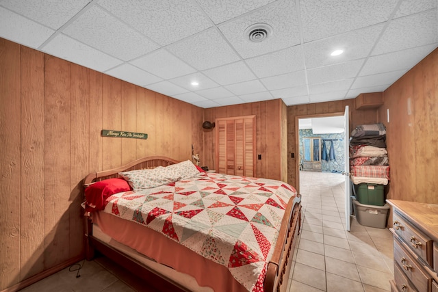 tiled bedroom featuring a drop ceiling, a closet, and wooden walls