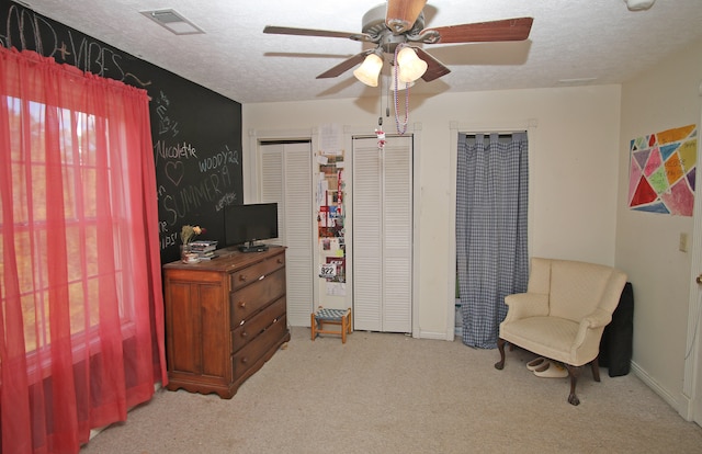 living area featuring light carpet, a textured ceiling, and ceiling fan