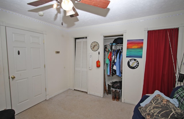 bedroom featuring ceiling fan, light carpet, a textured ceiling, and two closets