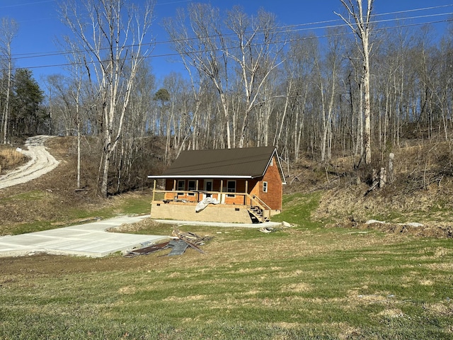 view of front facade with a forest view, a porch, concrete driveway, and a front yard