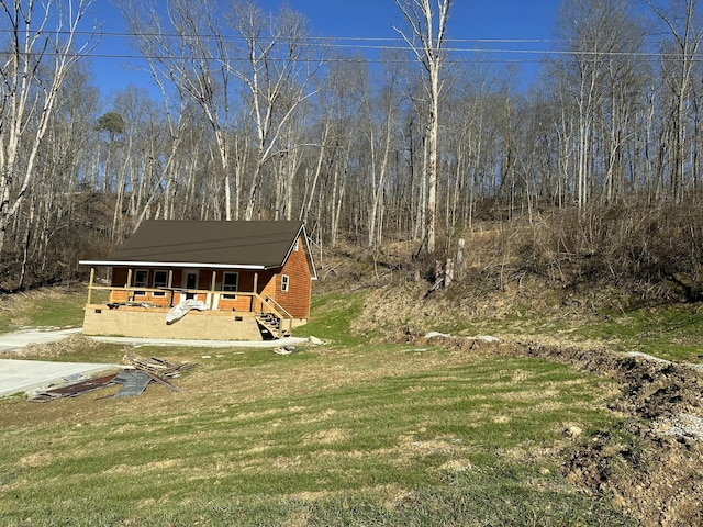 view of front of home featuring a front lawn, a porch, and a wooded view