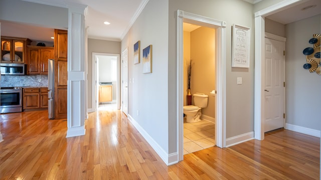 hallway featuring ornate columns, ornamental molding, and light wood-type flooring