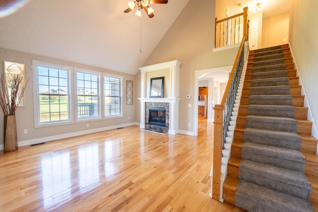 unfurnished living room with light hardwood / wood-style floors, high vaulted ceiling, ceiling fan, and a premium fireplace