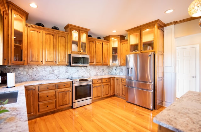 kitchen with backsplash, ornamental molding, appliances with stainless steel finishes, light hardwood / wood-style floors, and light stone counters