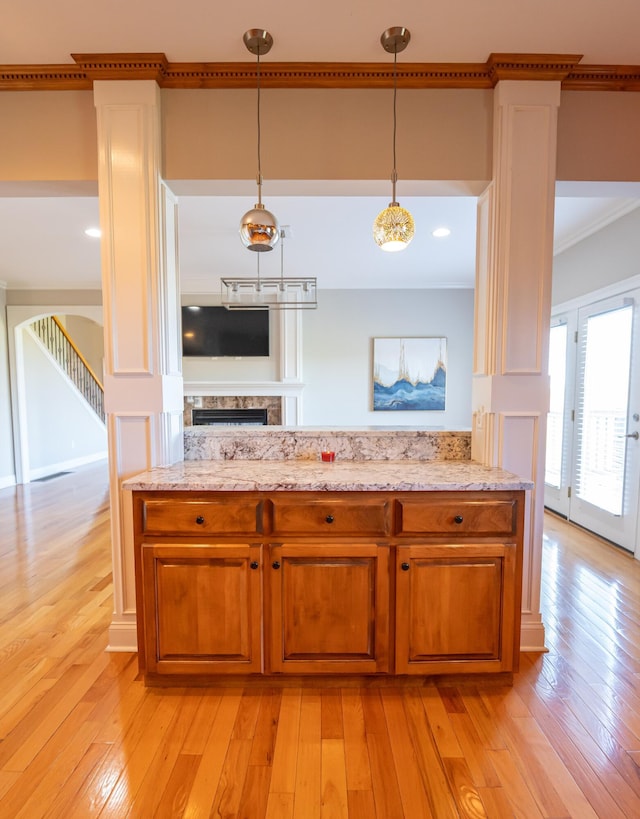 kitchen with pendant lighting, light hardwood / wood-style floors, light stone countertops, and crown molding