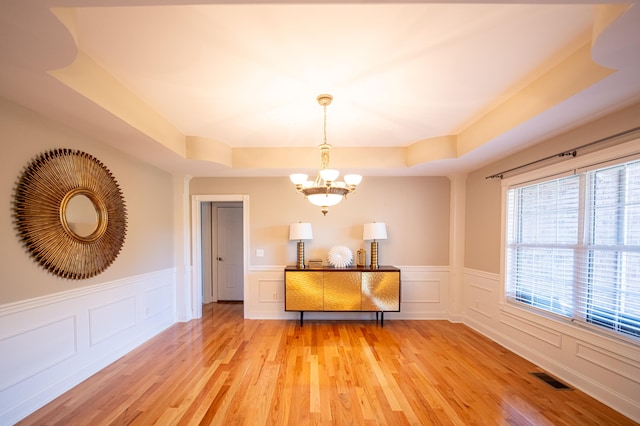 unfurnished dining area featuring hardwood / wood-style flooring, an inviting chandelier, and a tray ceiling