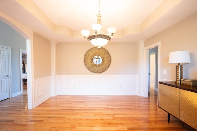 unfurnished dining area featuring a tray ceiling, light hardwood / wood-style floors, and a notable chandelier