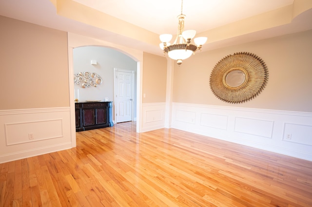 unfurnished room with a raised ceiling, light hardwood / wood-style flooring, and an inviting chandelier