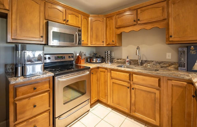 kitchen featuring light stone countertops, appliances with stainless steel finishes, light tile patterned floors, and sink