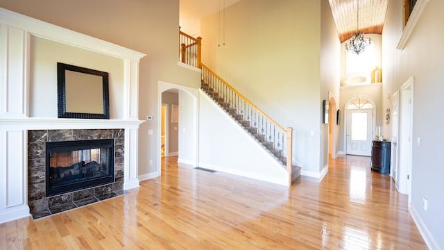 unfurnished living room featuring a fireplace, hardwood / wood-style floors, a towering ceiling, and a notable chandelier