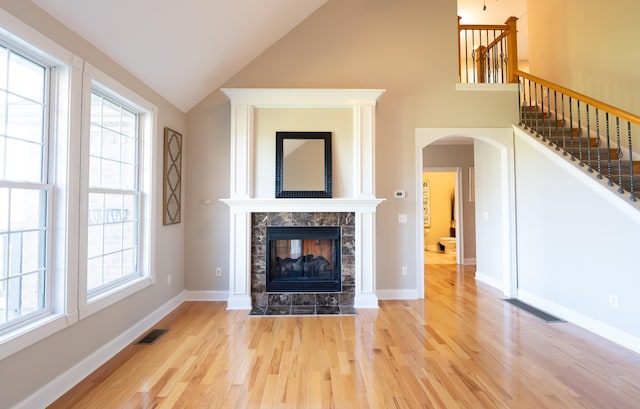 unfurnished living room featuring a tile fireplace, plenty of natural light, high vaulted ceiling, and light hardwood / wood-style floors