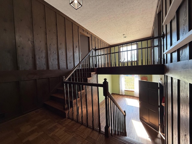 stairway with a textured ceiling and wood walls