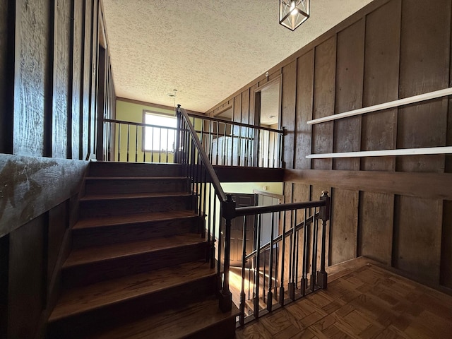 stairs with parquet floors, wood walls, and a textured ceiling