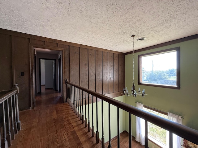 hall featuring a textured ceiling, a notable chandelier, dark hardwood / wood-style floors, and wood walls