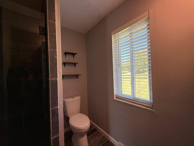 bathroom with toilet, a textured ceiling, and a shower with shower door