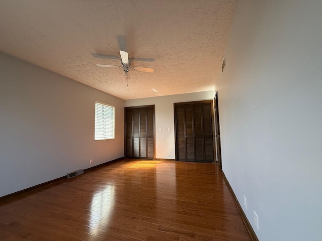 unfurnished bedroom featuring ceiling fan, a textured ceiling, two closets, and hardwood / wood-style floors