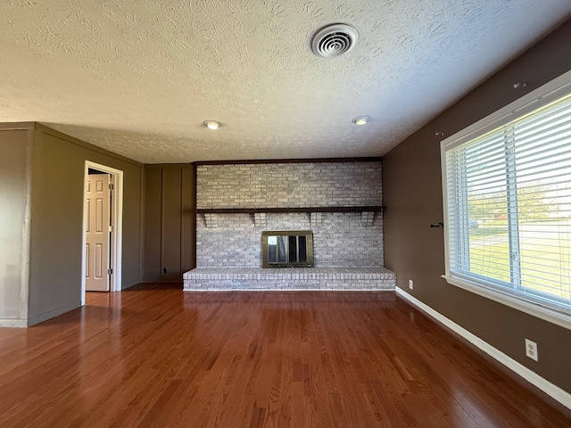 unfurnished living room with a brick fireplace, a textured ceiling, and dark hardwood / wood-style flooring