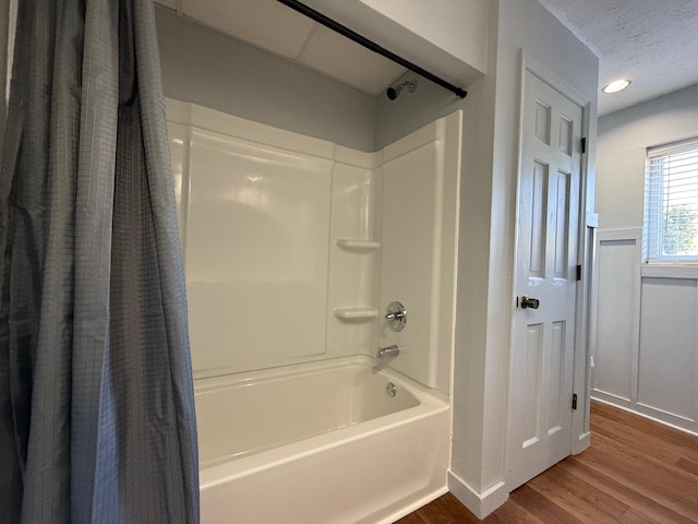 bathroom with a textured ceiling, hardwood / wood-style flooring, and shower / bathtub combination with curtain