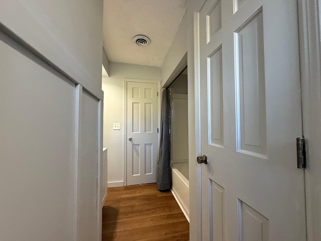 hallway with a textured ceiling and wood-type flooring