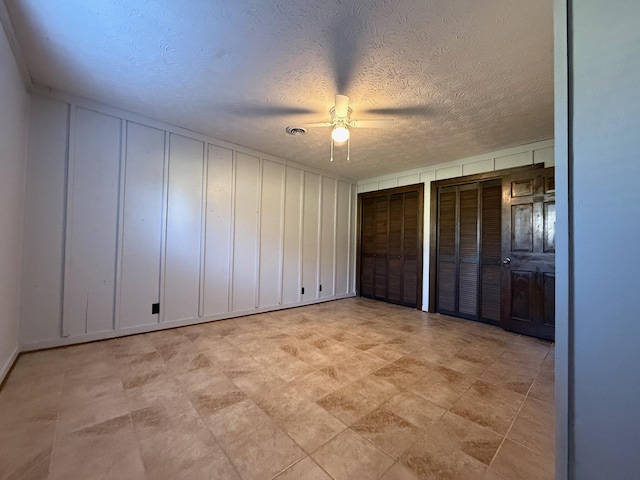 unfurnished bedroom featuring two closets, a textured ceiling, and ceiling fan