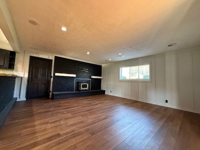 unfurnished living room featuring a wood stove, a textured ceiling, and hardwood / wood-style flooring