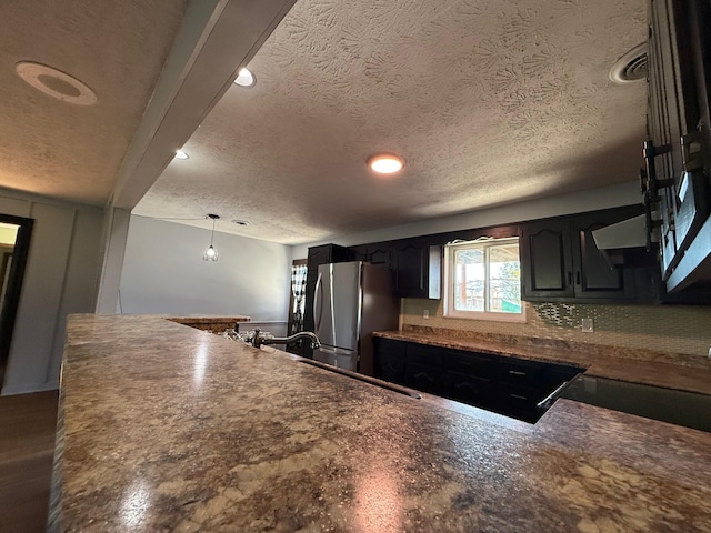 kitchen with backsplash, a textured ceiling, hanging light fixtures, stainless steel fridge, and beamed ceiling