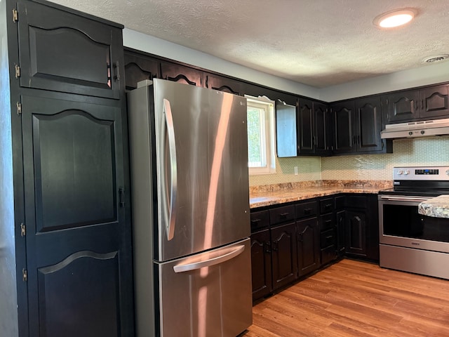 kitchen with decorative backsplash, light stone counters, a textured ceiling, light hardwood / wood-style floors, and stainless steel appliances