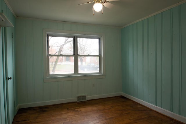 empty room with ornamental molding, dark wood-type flooring, and ceiling fan