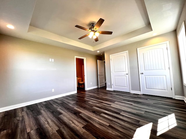 unfurnished bedroom with dark hardwood / wood-style flooring, ceiling fan, and a raised ceiling