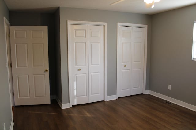 unfurnished bedroom featuring two closets, dark hardwood / wood-style floors, and ceiling fan