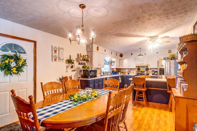 dining space with ceiling fan with notable chandelier, light hardwood / wood-style flooring, and a textured ceiling