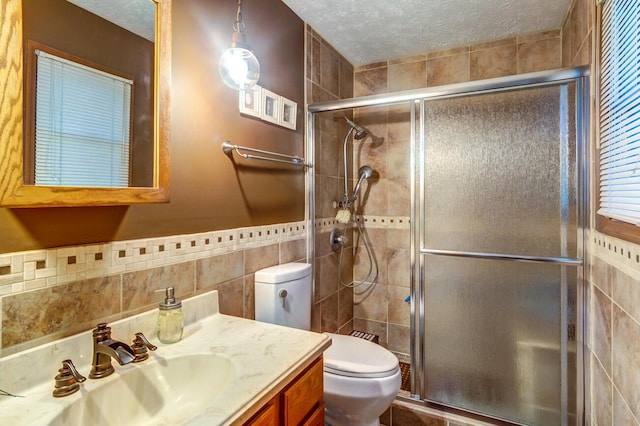 bathroom featuring a shower with shower door, tile walls, vanity, toilet, and a textured ceiling