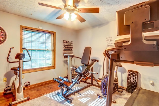 workout room with ceiling fan, light wood-type flooring, and a textured ceiling