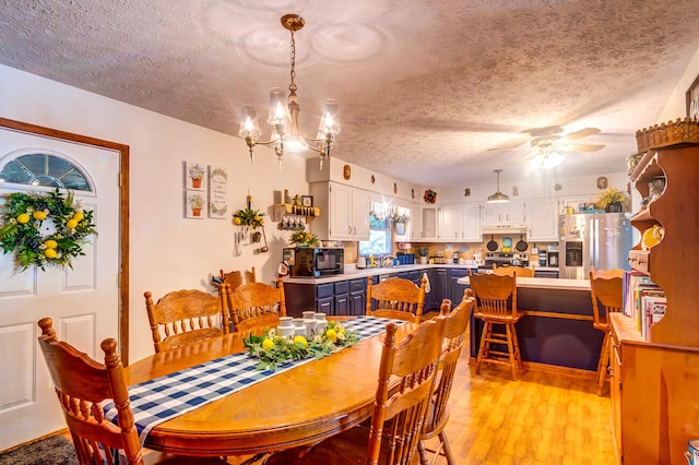 dining room featuring light hardwood / wood-style flooring, a textured ceiling, sink, and ceiling fan with notable chandelier