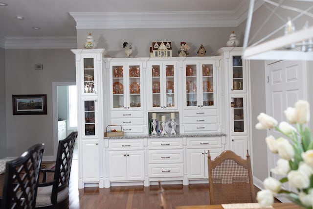 bar with light stone countertops, crown molding, white cabinets, and dark hardwood / wood-style flooring