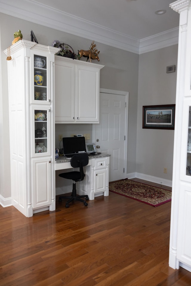 unfurnished office featuring ornamental molding, built in desk, and dark wood-type flooring