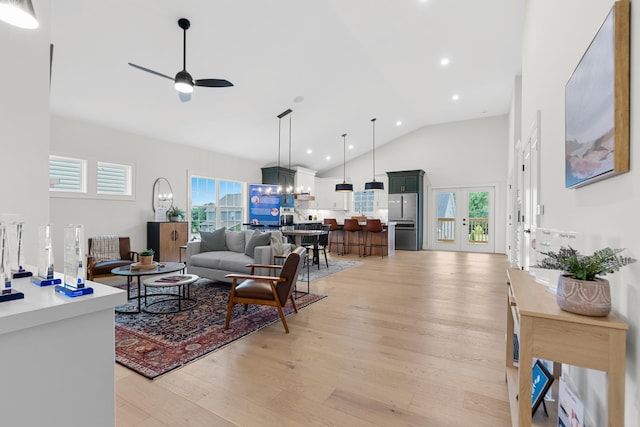 living room with a healthy amount of sunlight, high vaulted ceiling, ceiling fan with notable chandelier, and light wood-type flooring