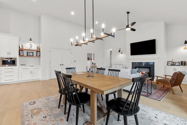 dining area with light hardwood / wood-style floors, a premium fireplace, high vaulted ceiling, and ceiling fan